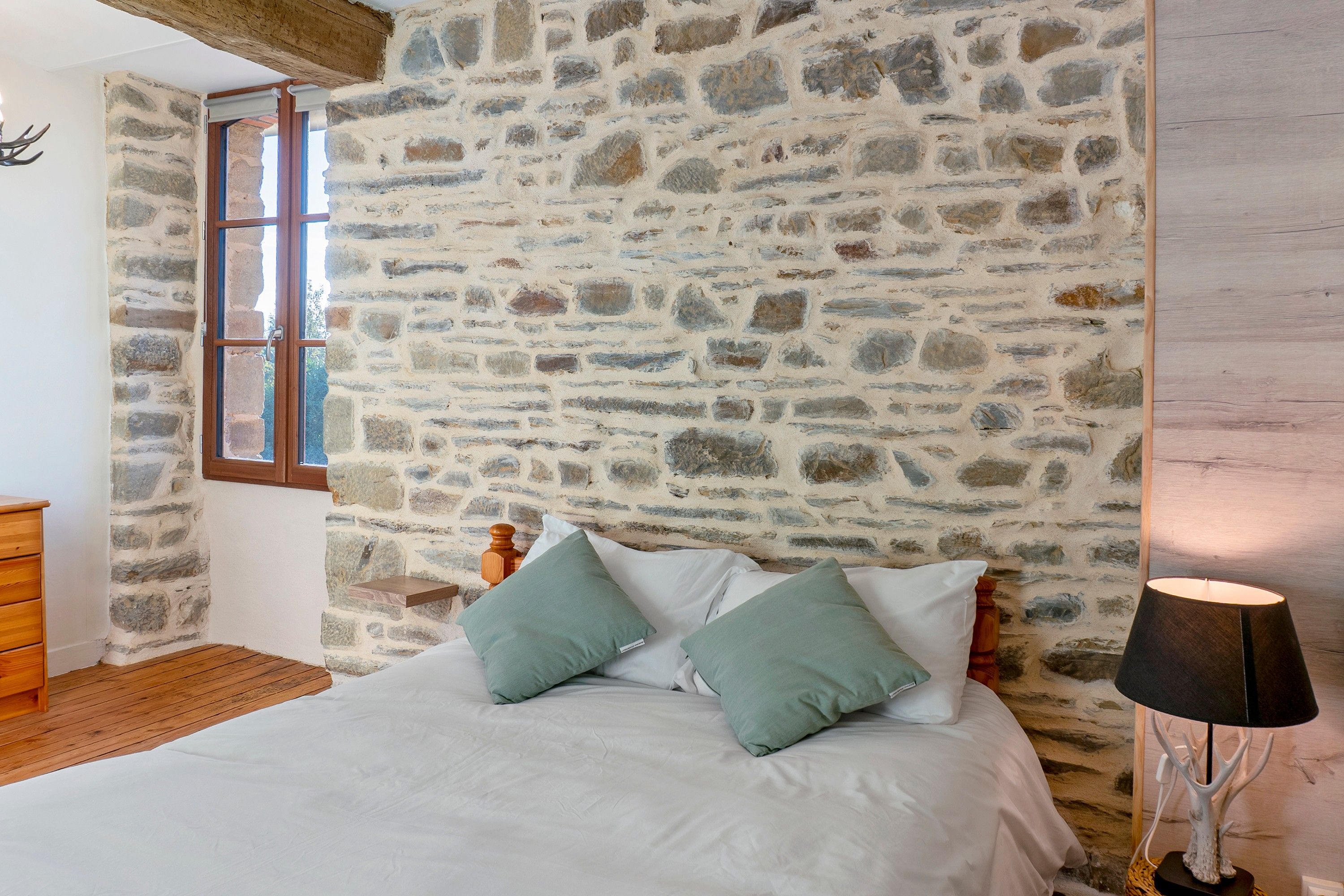 Une chambre avec un mur en pierre, un cadre de lit en bois et une table de chevet.