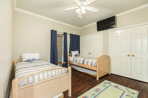 Ein Schlafzimmer mit zwei Einzelbetten, einem Deckenventilator, einem Fernseher und einer Doppeltür.