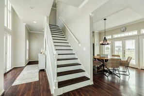 A staircase with dark wooden steps and white railings, leading to a dining area with wicker chairs and a chandelier. - Spacious Bayfront Retreat - Pet Friendly with Private Fishing Pier (Galveston)