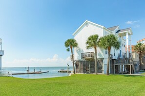 A beachfront property with a white building, a dock, and a clear sky. - Spacious Bayfront Retreat - Pet Friendly with Private Fishing Pier (Galveston)