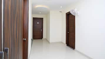 Un pasillo con una puerta de madera a la izquierda, una puerta blanca en el centro y una pared blanca con un ventilador de techo a la derecha.