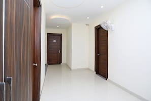 Un pasillo con una puerta de madera a la izquierda, una puerta blanca en el centro y una pared blanca con un ventilador de techo a la derecha.