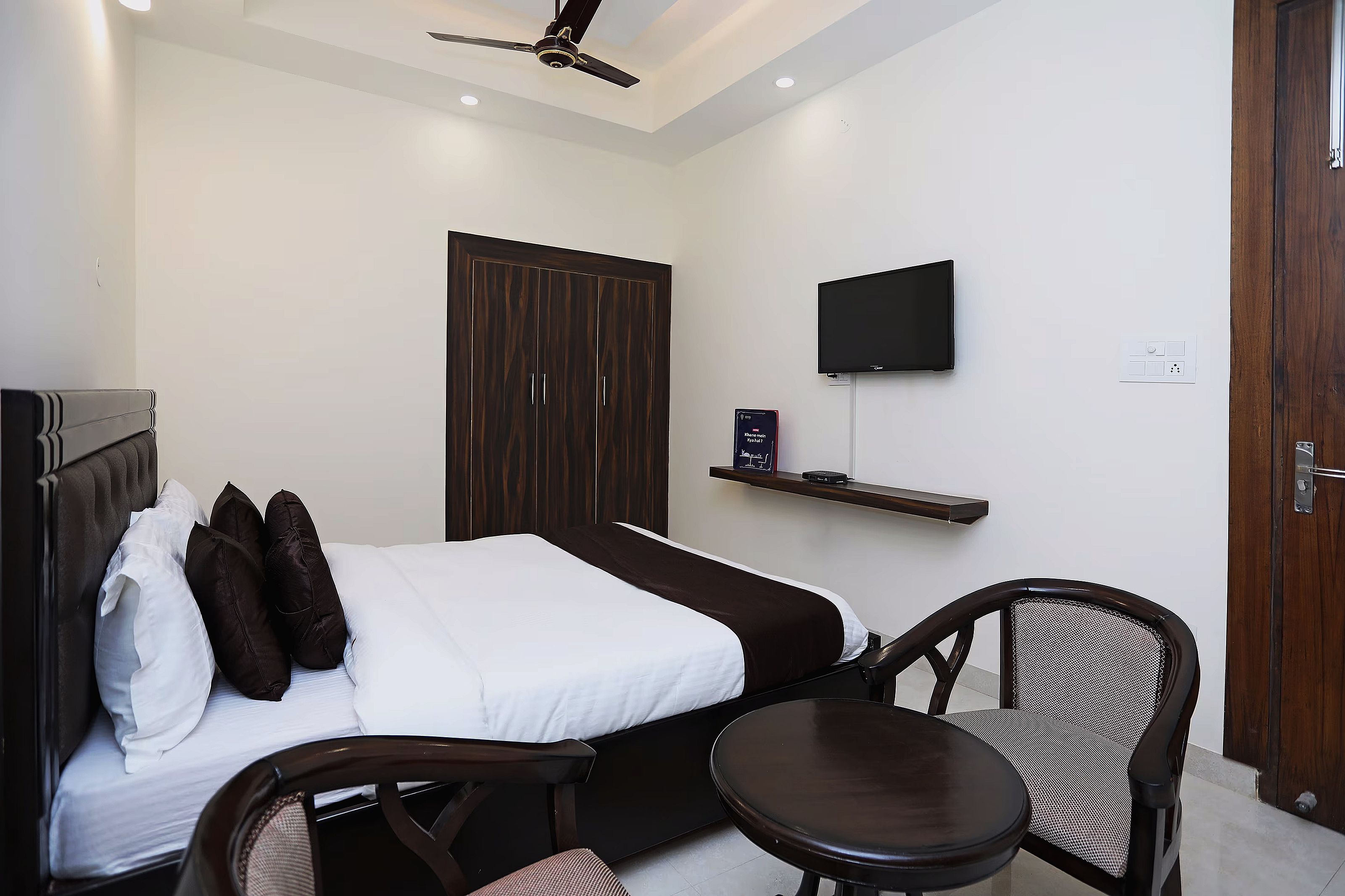 A hotel room with a bed, a chair, a TV, and a wardrobe.