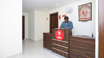 Bancada de recepção com logotipo, uma pessoa em pé atrás dela, um quadro na parede e uma porta ao fundo.