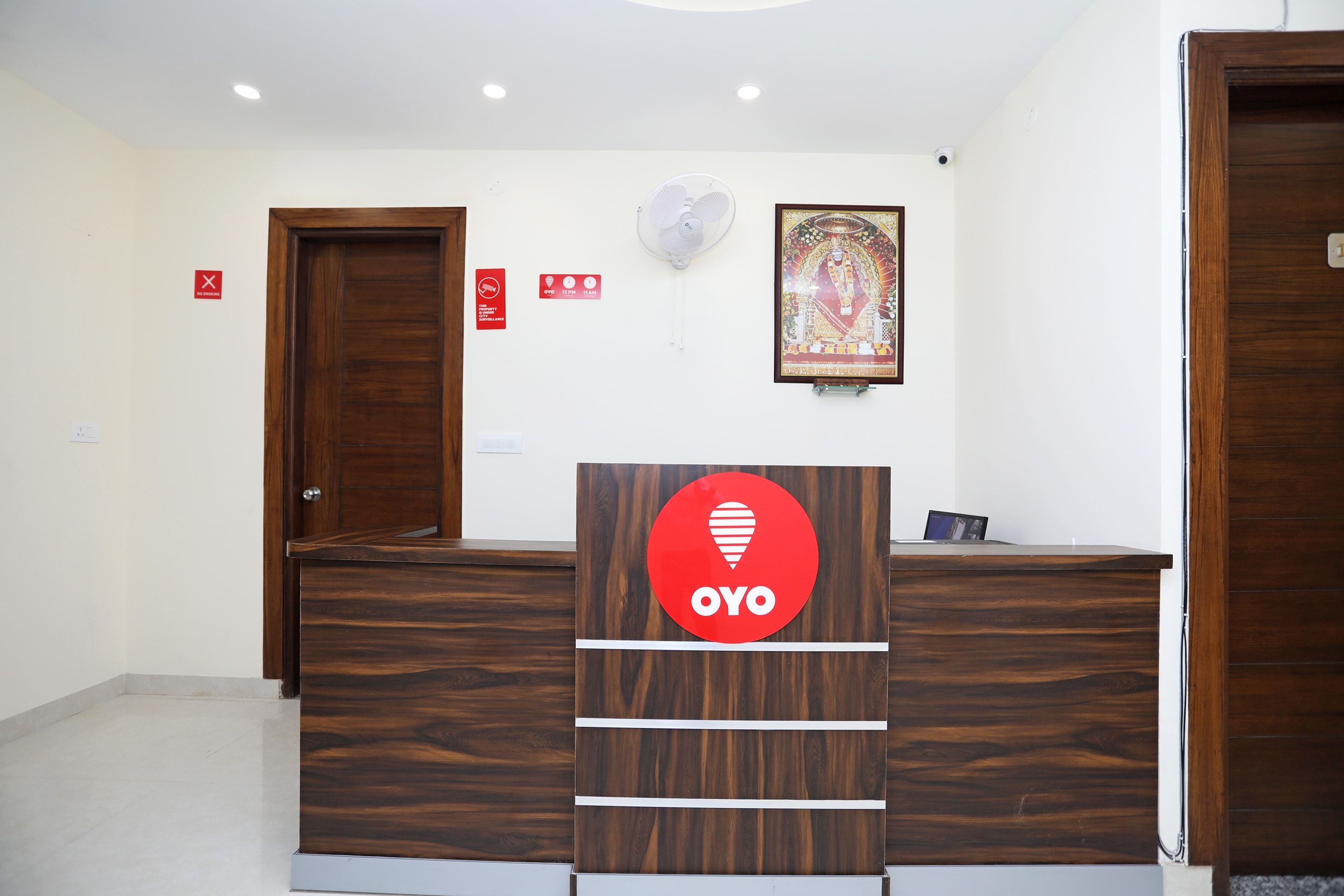 A reception desk with a wooden finish, a framed religious artwork on the wall, and a 'No Smoking' sign.