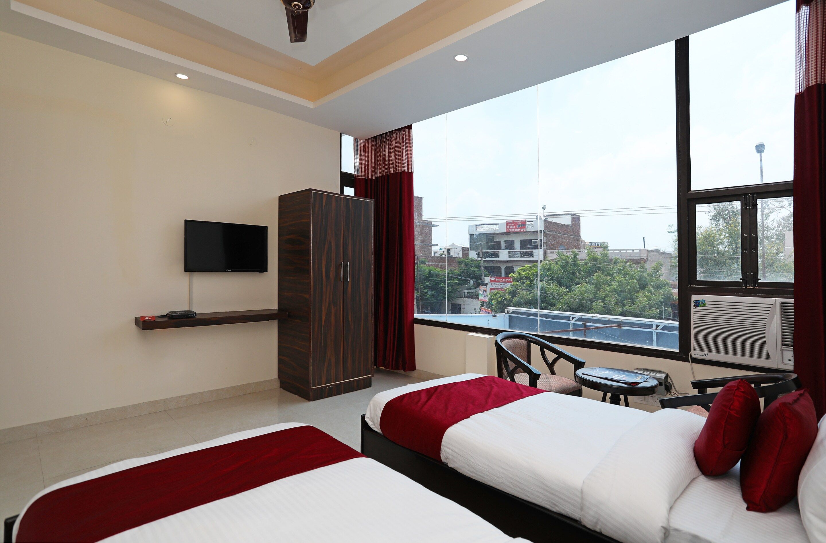 Quarto de hotel com duas camas, televisão, guarda-roupa, janela com vista para a cidade e ar condicionado.