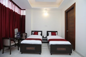 A hotel room with two single beds, a desk with a chair, a wooden door, and a ceiling light.