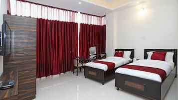 A hotel room with two beds, a desk, a chair, a TV, and a window with red curtains.
