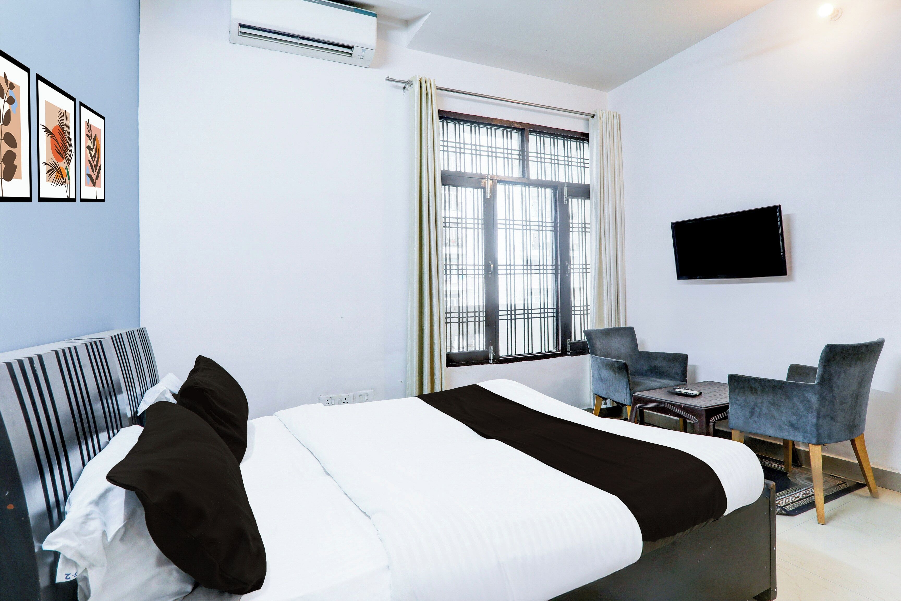 Habitación de hotel con cama, escritorio, dos sillas, televisor y ventana con persianas.