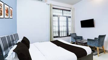 Habitación de hotel con cama, escritorio, dos sillas, televisor y ventana con persianas.