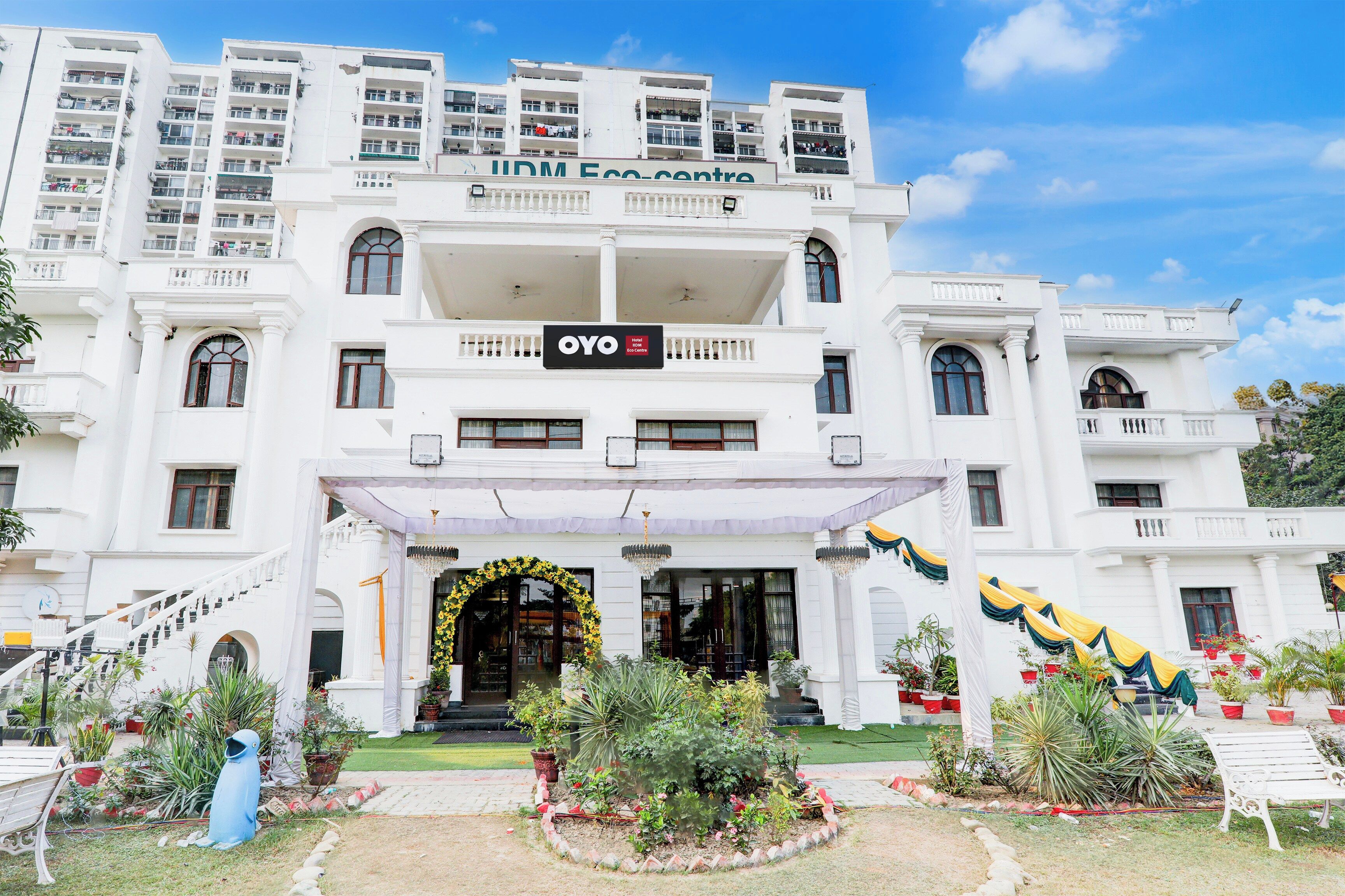 Un hotel de varios pisos con entrada central, balcones y un jardín con plantas en macetas.