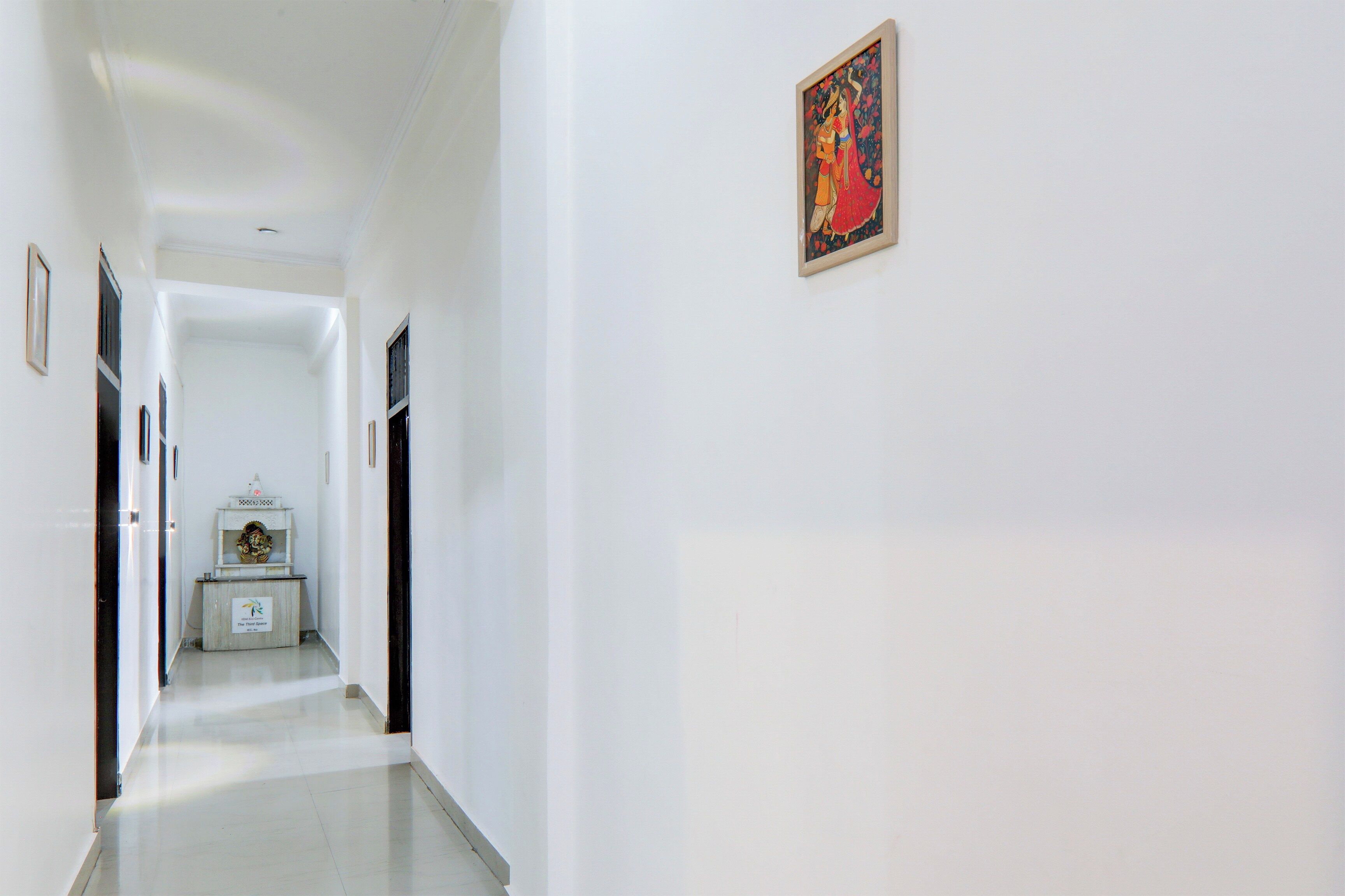 A hallway with a framed painting on the wall, a small shrine with a statue, and a sign indicating a 'Prayer and Space' area.