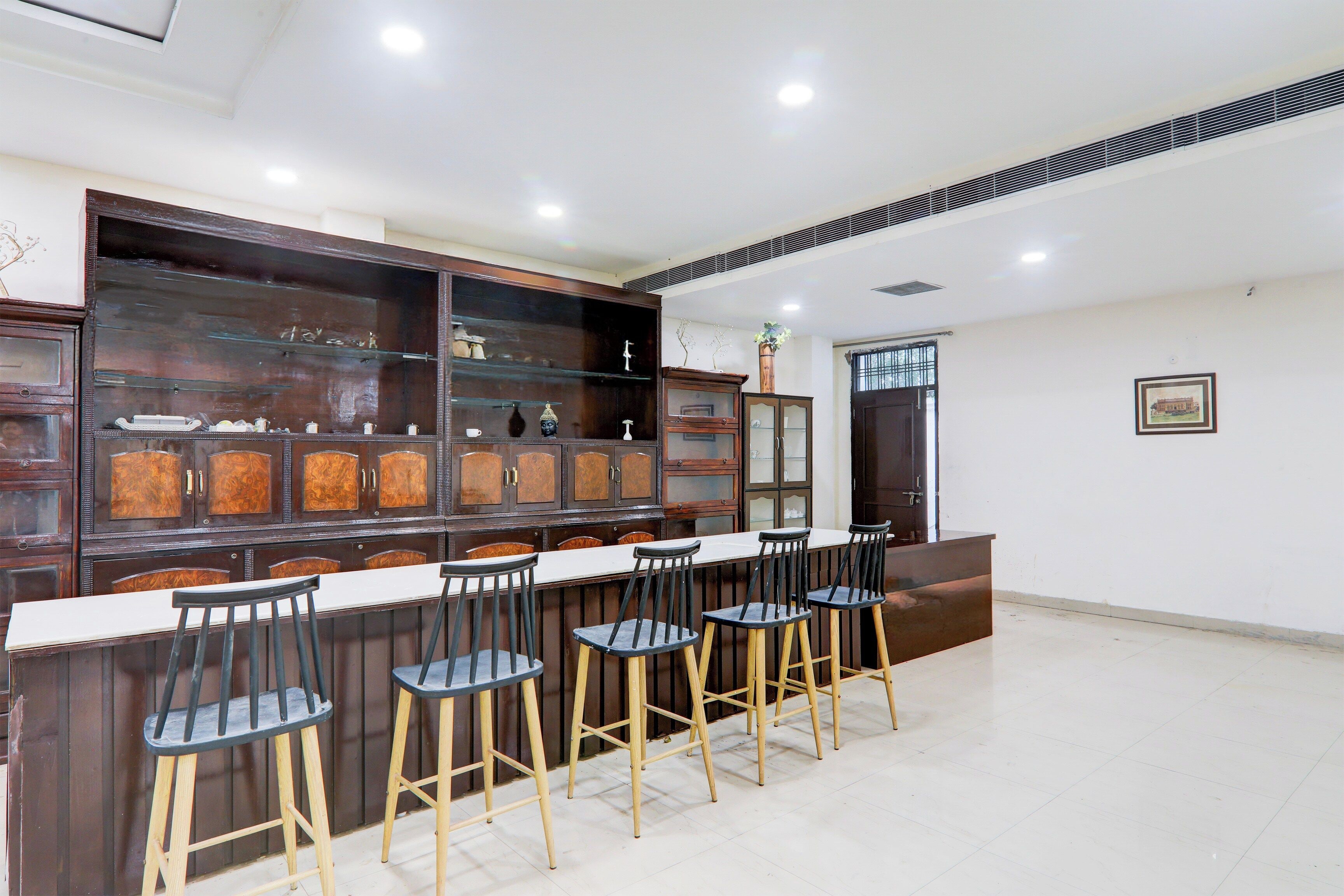 Zona de bar con una barra alargada y varios taburetes, un armario de madera con puertas de cristal y una puerta con ventanal.
