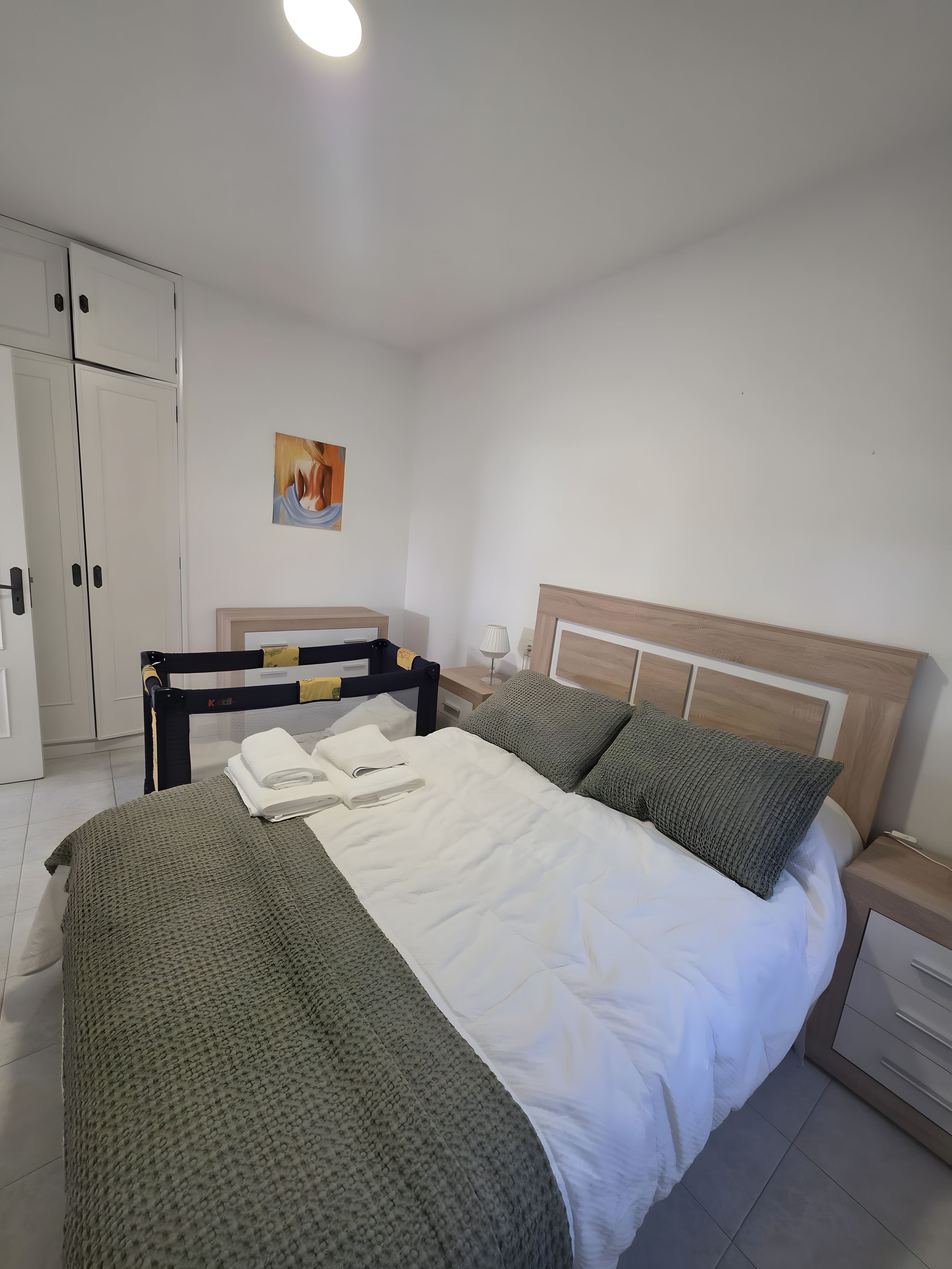 Una camera da letto con un letto, un comodino, una lampada, un armadio e un quadro appeso al muro.