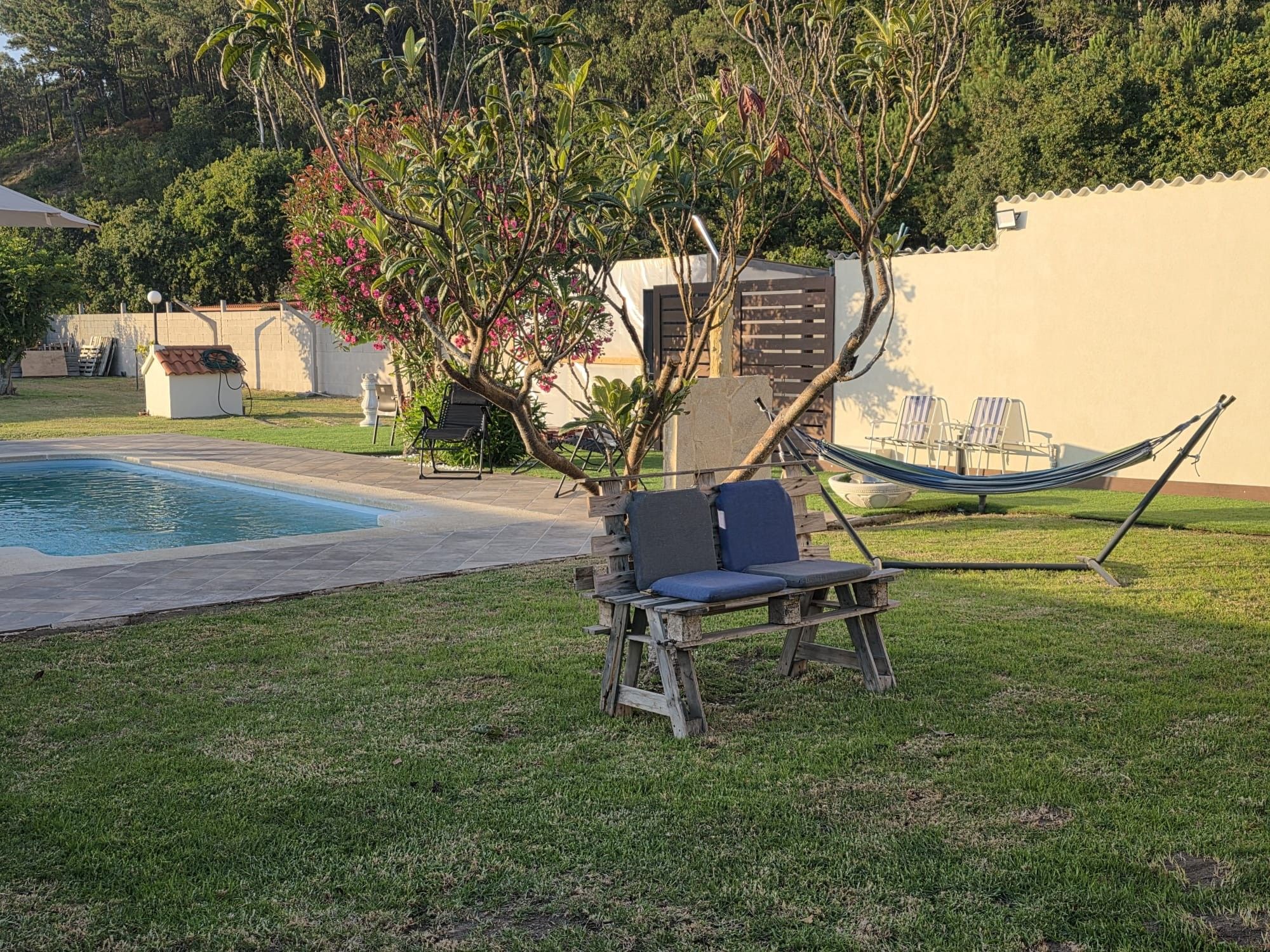 Un área junto a la piscina con una hamaca, un banco de madera y una silla.