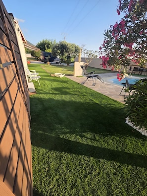 A backyard with a swimming pool, a grassy lawn, and a patio area.