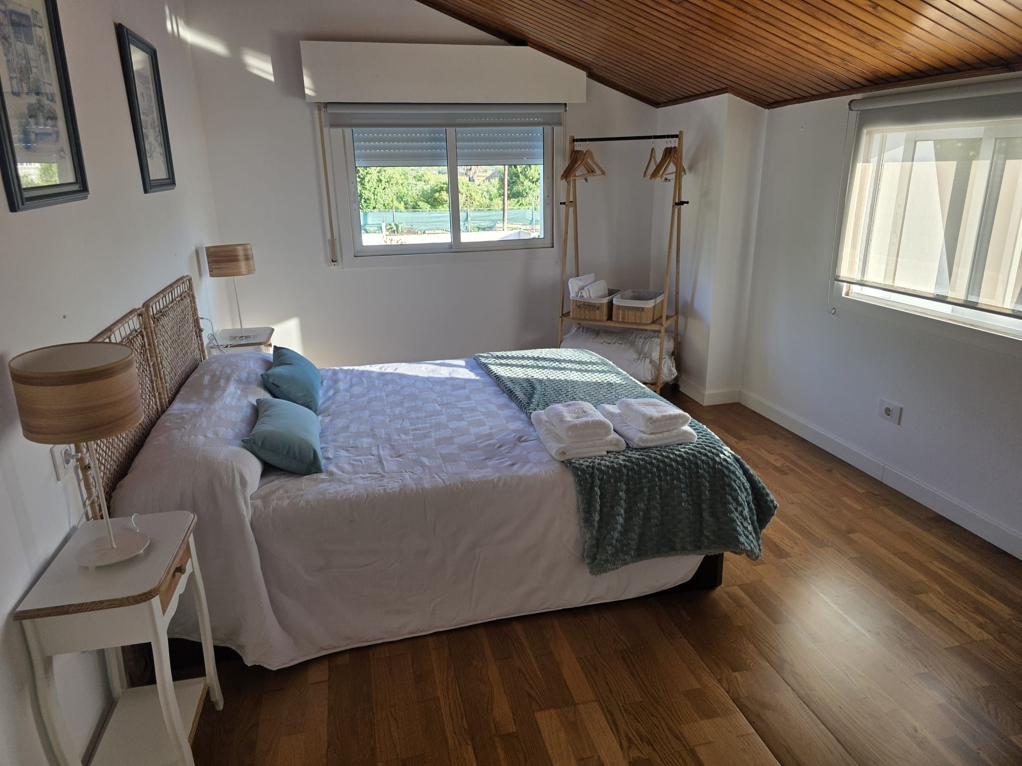 A bedroom with a bed, bedside table, lamp, and a window with a view of greenery.