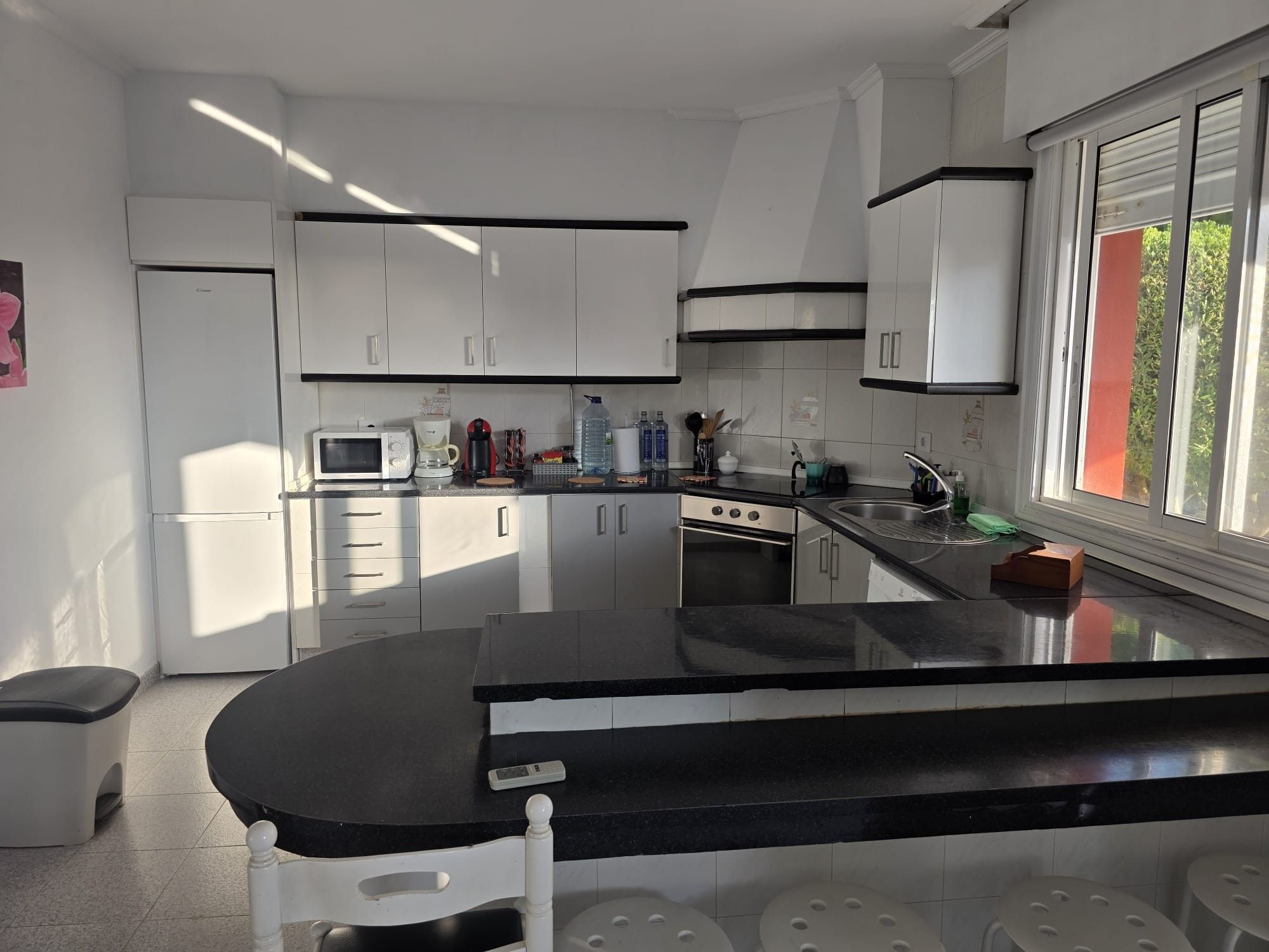 A modern kitchen with white cabinets, a black countertop, and a window with a view of greenery.