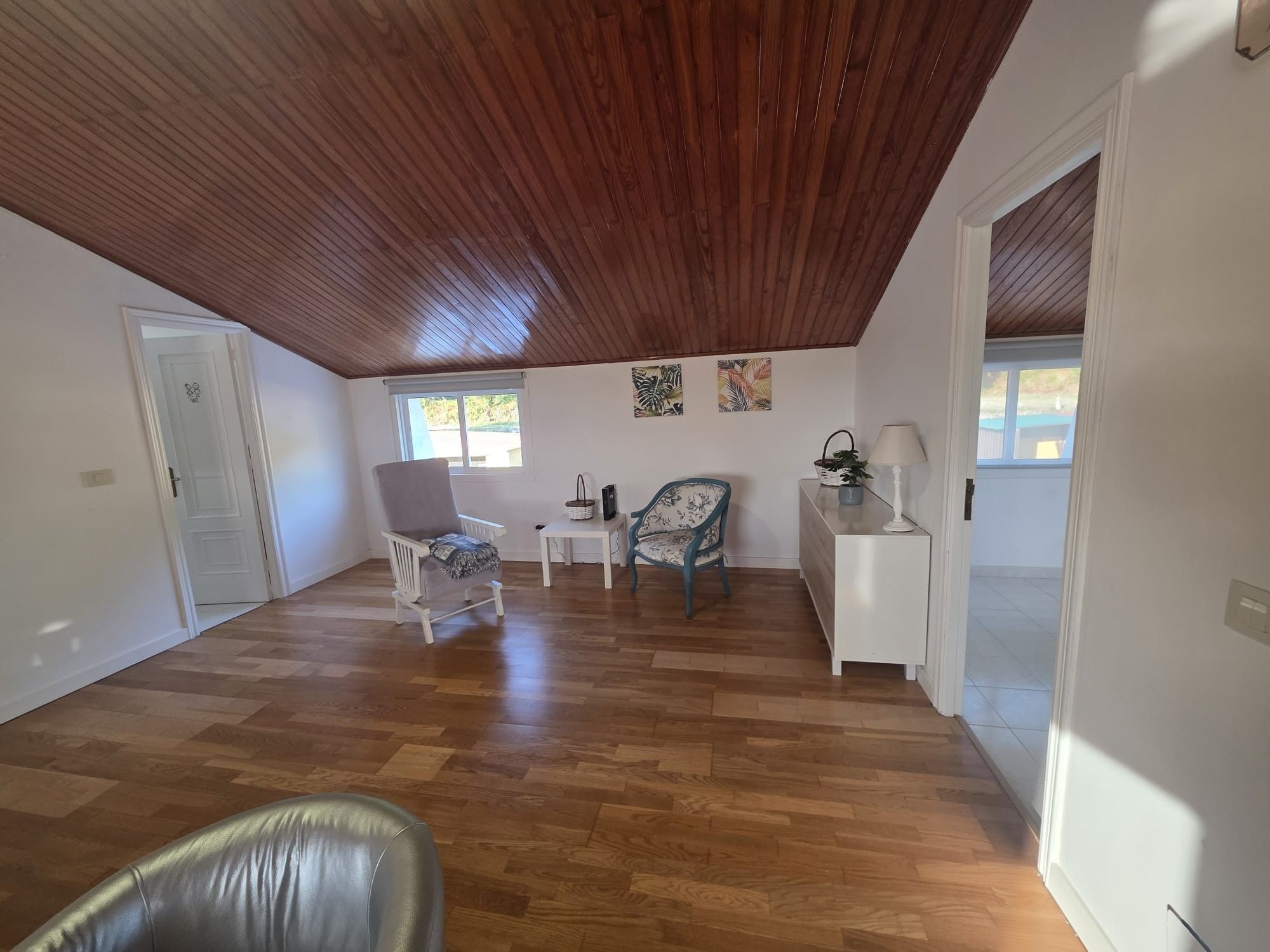 A spacious room with wooden flooring, a white door, a grey armchair, a small table, and a decorative chair.