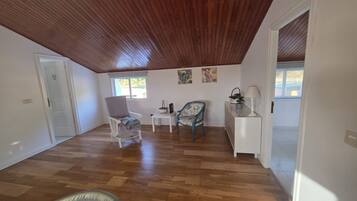 A spacious room with wooden flooring, a white door, a grey armchair, a small table, and a decorative chair.