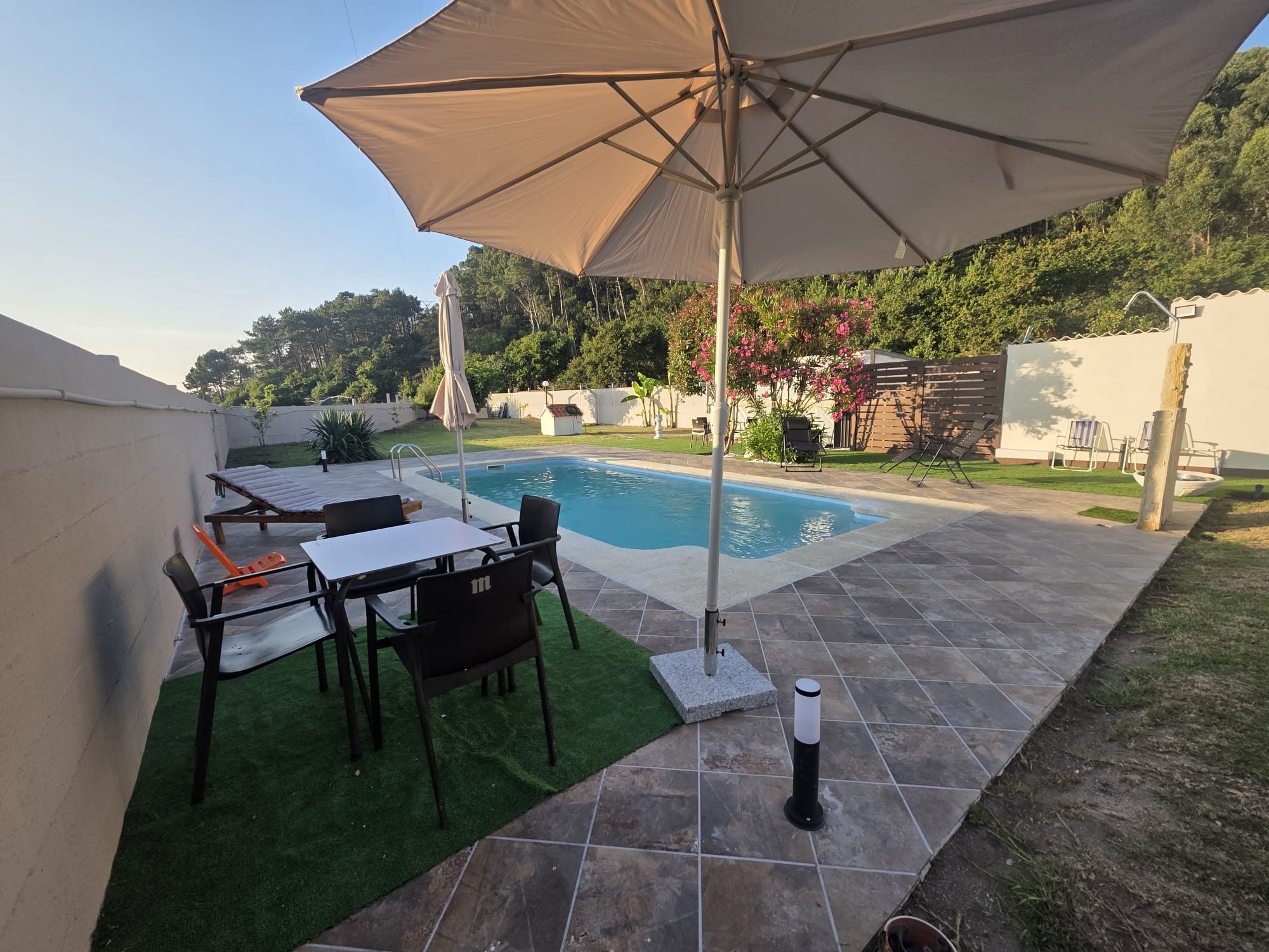 A backyard with a swimming pool, a covered patio area, and outdoor furniture.