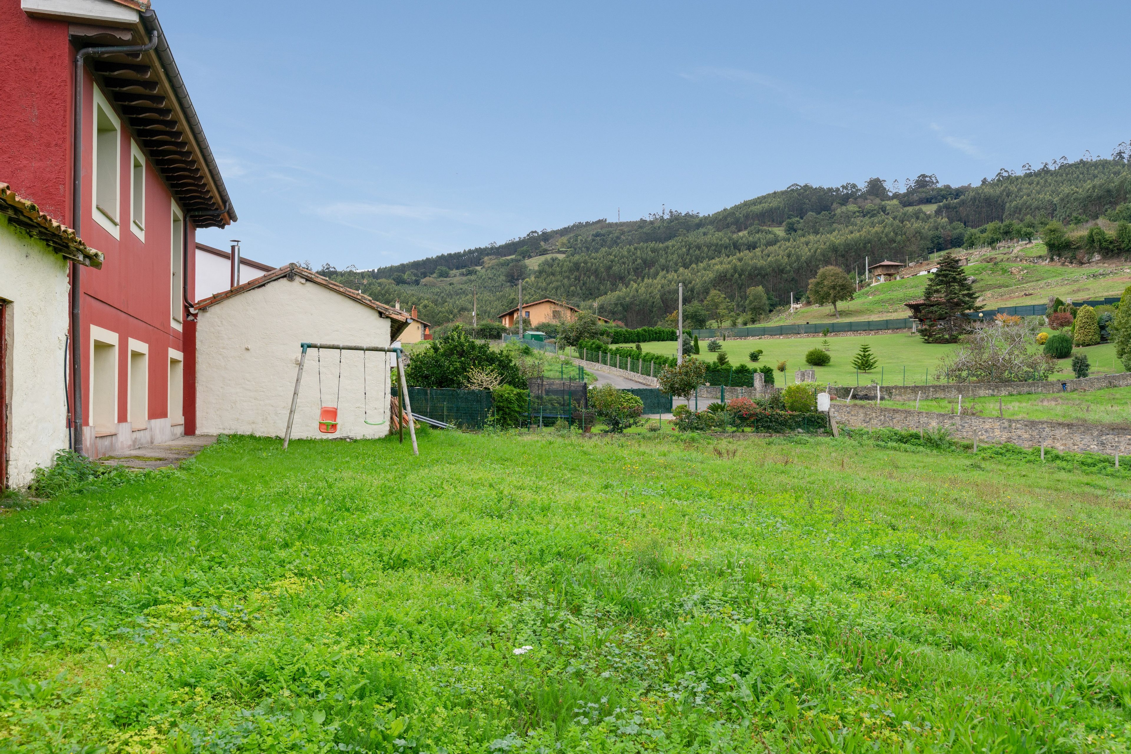 Paisaje rural con un edificio rojo, un campo cubierto de hierba y un paisaje montañoso al fondo.