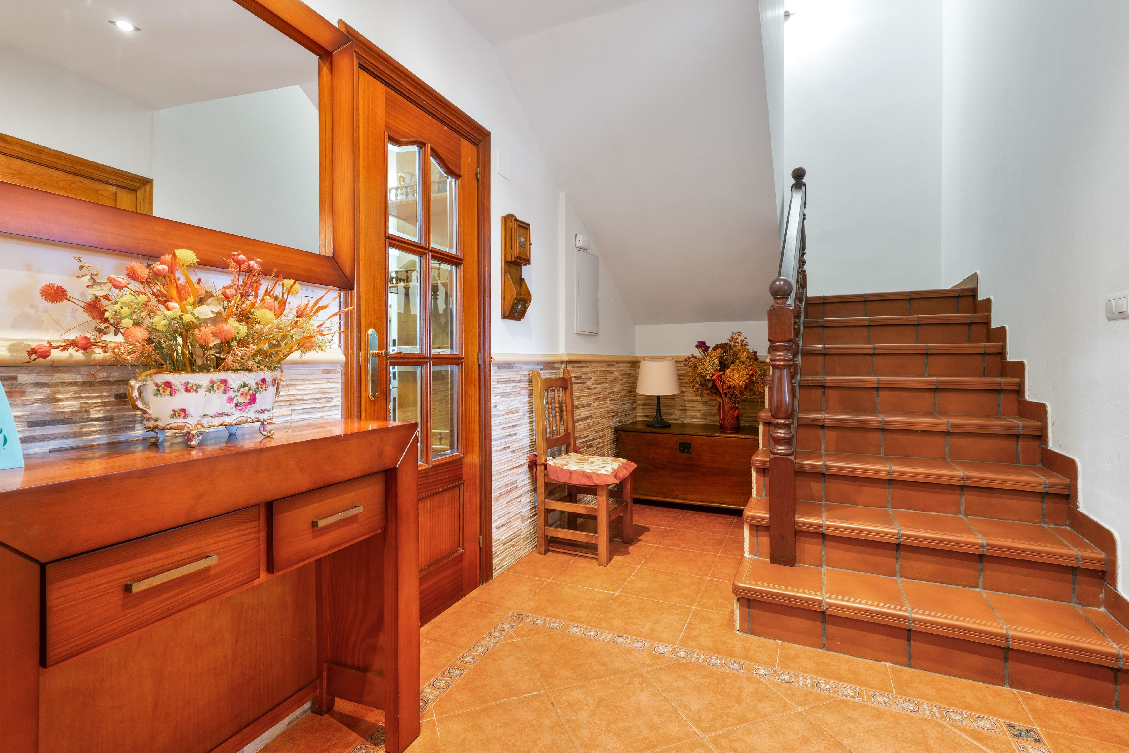 Un escalier en bois menant à un palier doté d’un sol carrelé, d’un banc en bois et d’une lampe fixée au mur.