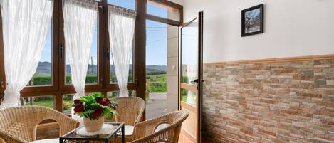 Ein Balkon mit Korbmöbeln, einem Tisch mit Blumenvase und Blick auf die Landschaft.