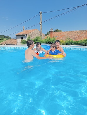 Una piscina con agua azul cristalina, bordeada por un revestimiento de azulejos, y un edificio con tejado de cerámica al fondo.