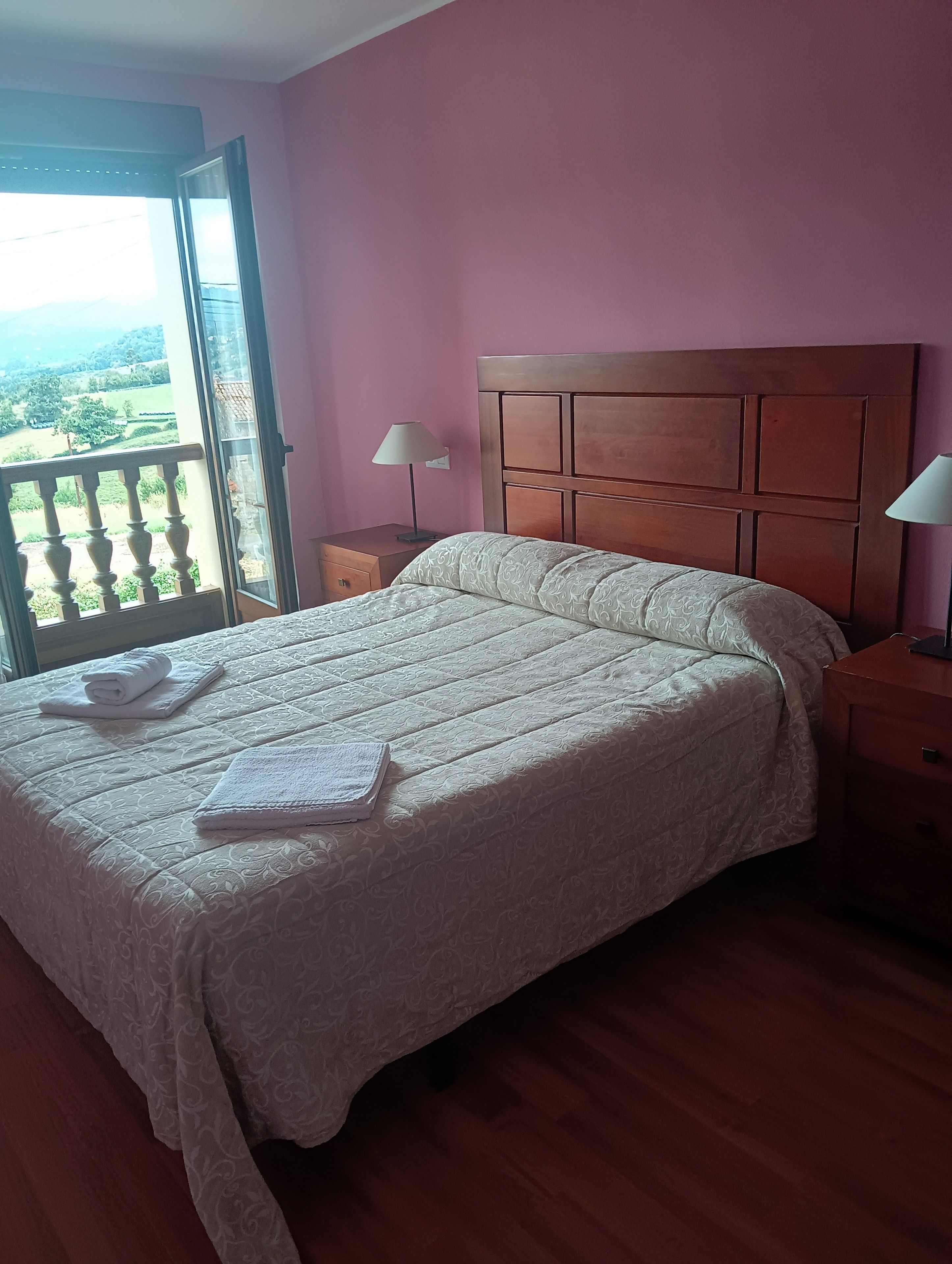Une chambre à coucher avec un grand lit, une tête de lit en bois, une table de chevet avec une lampe et une vue par la fenêtre.