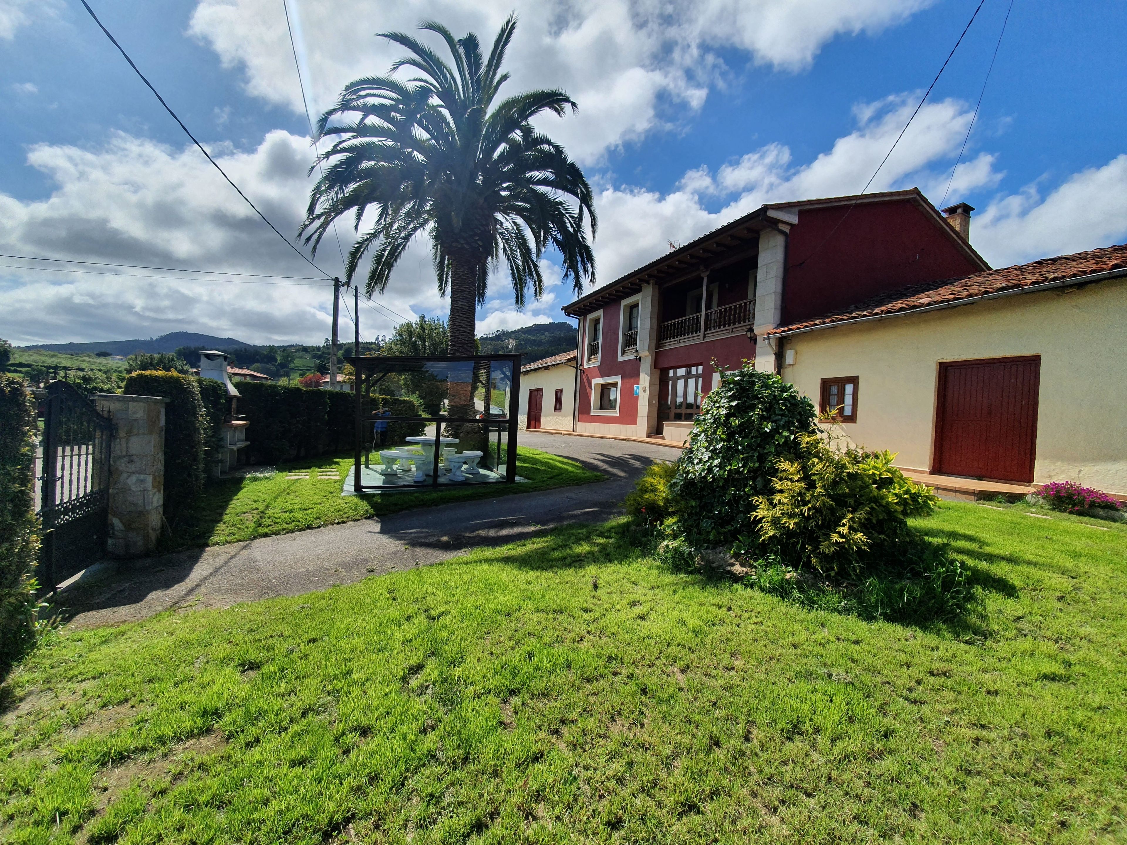 Una propiedad residencial con un césped cuidado, un área de comedor al aire libre con paredes de vidrio y una casa de dos pisos con techo rojo.