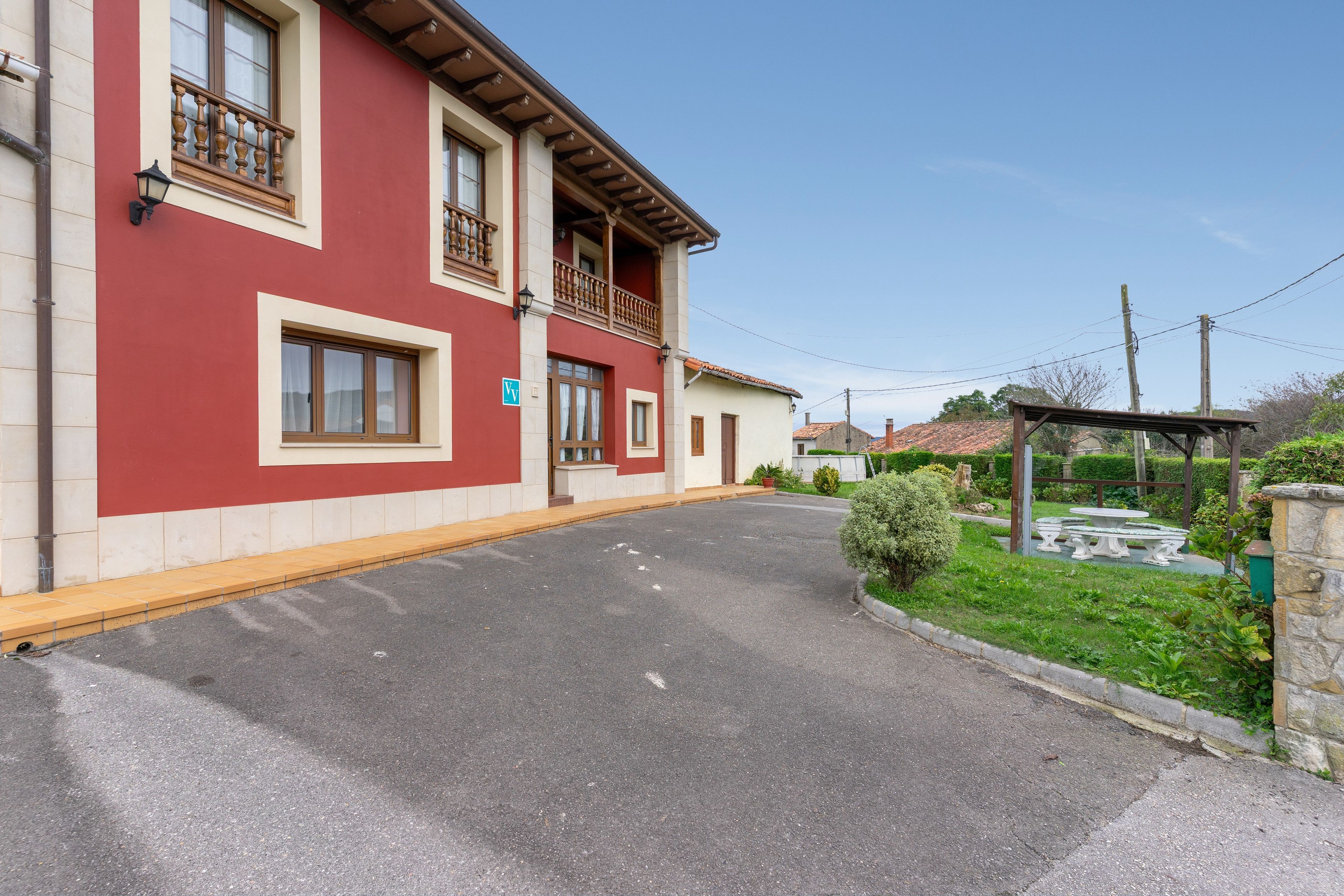 Un bâtiment à deux étages avec une façade rouge, un balcon et une allée pavée.