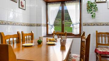 Un comedor con una mesa de madera, sillas y vistas a un paisaje verde a través de una ventana con cortinas.