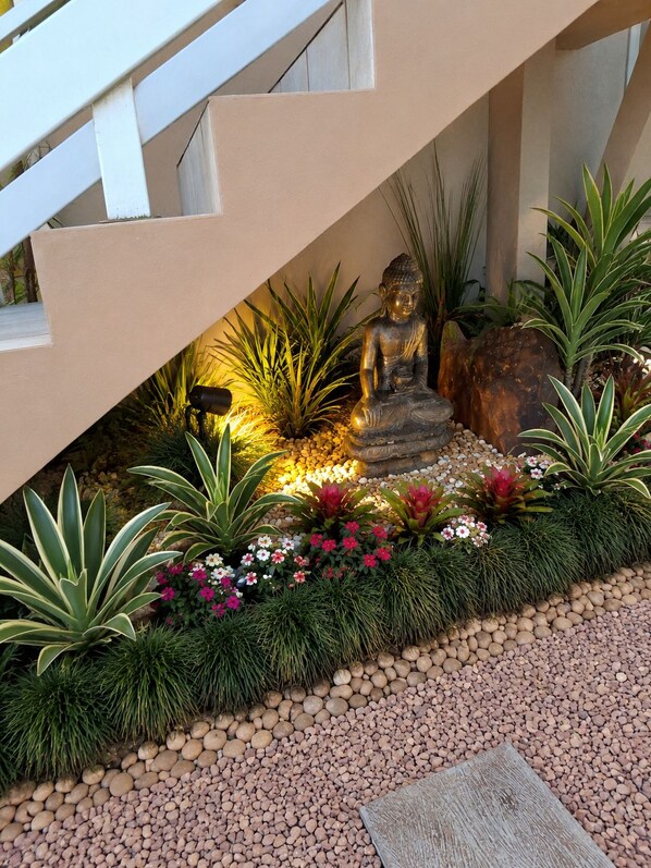 A Buddha statue under a staircase, surrounded by a garden with various plants and flowers. - New Listing (Bento Gonçalves)