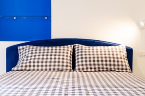 A bed with a checkered bedspread and pillows, a blue upholstered headboard, and a blue wall. - [Cozy] Blue Velvet Loft* (Torino)
