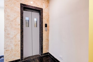 Un pasillo con pared de mármol, una puerta con ventanilla y un portero automático en la pared.