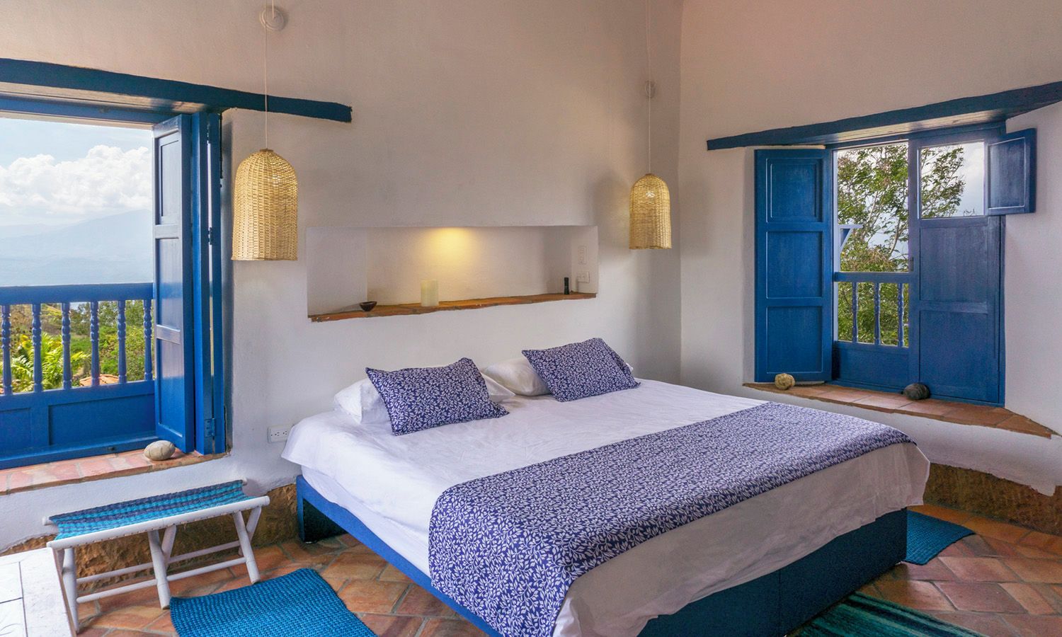 Un dormitorio con cama, almohadas, una mesita de noche, estante y ventana con vistas.