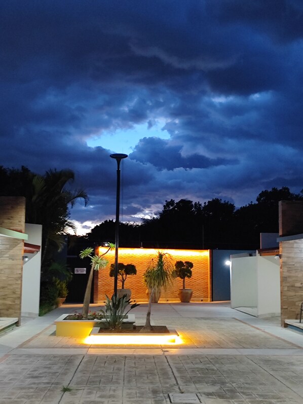 An outdoor area with a paved walkway, potted plants, and a building with a warm-lit wall. - Dpas 82 (Tlalixtac de Cabrera)