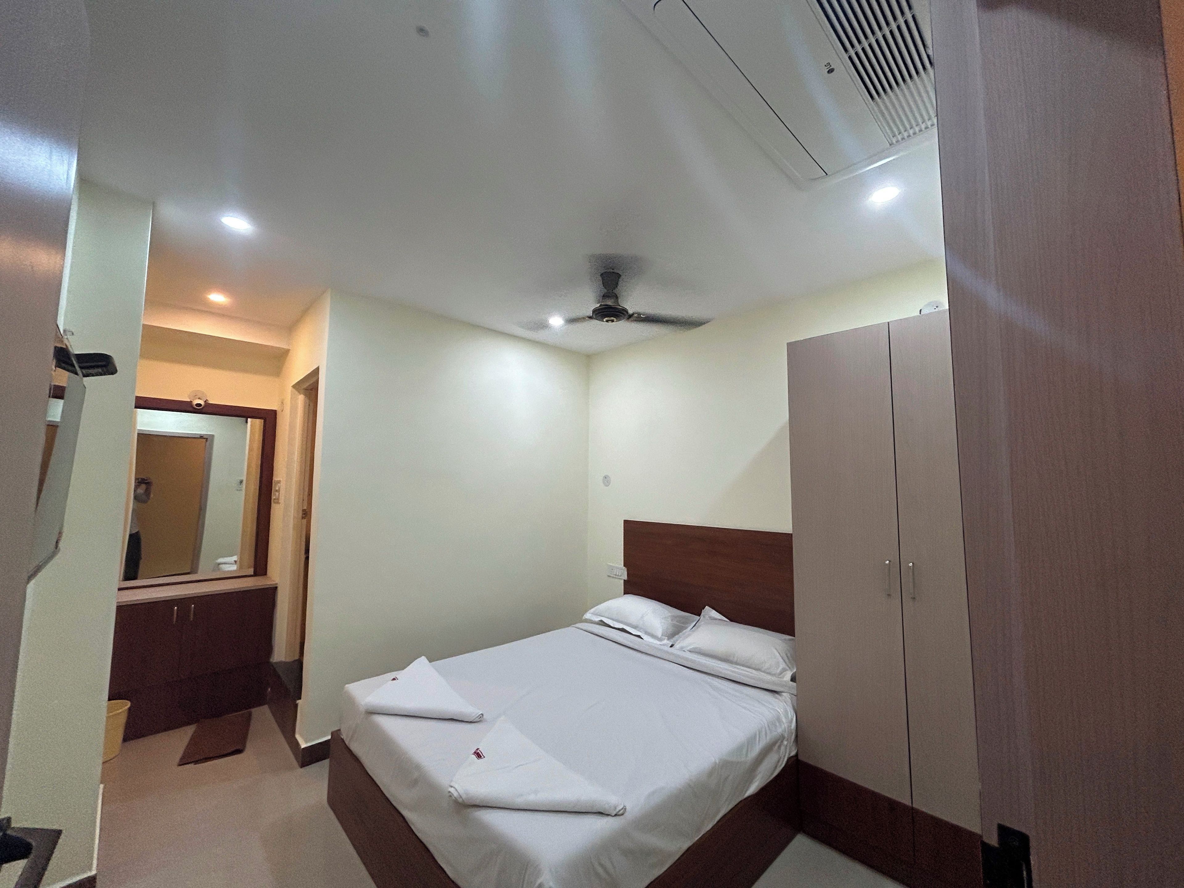 Una habitación de hotel con cama, armario, espejo y ventilador de techo.