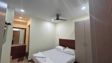 A hotel room with a bed, a wardrobe, a mirror, and a ceiling fan.