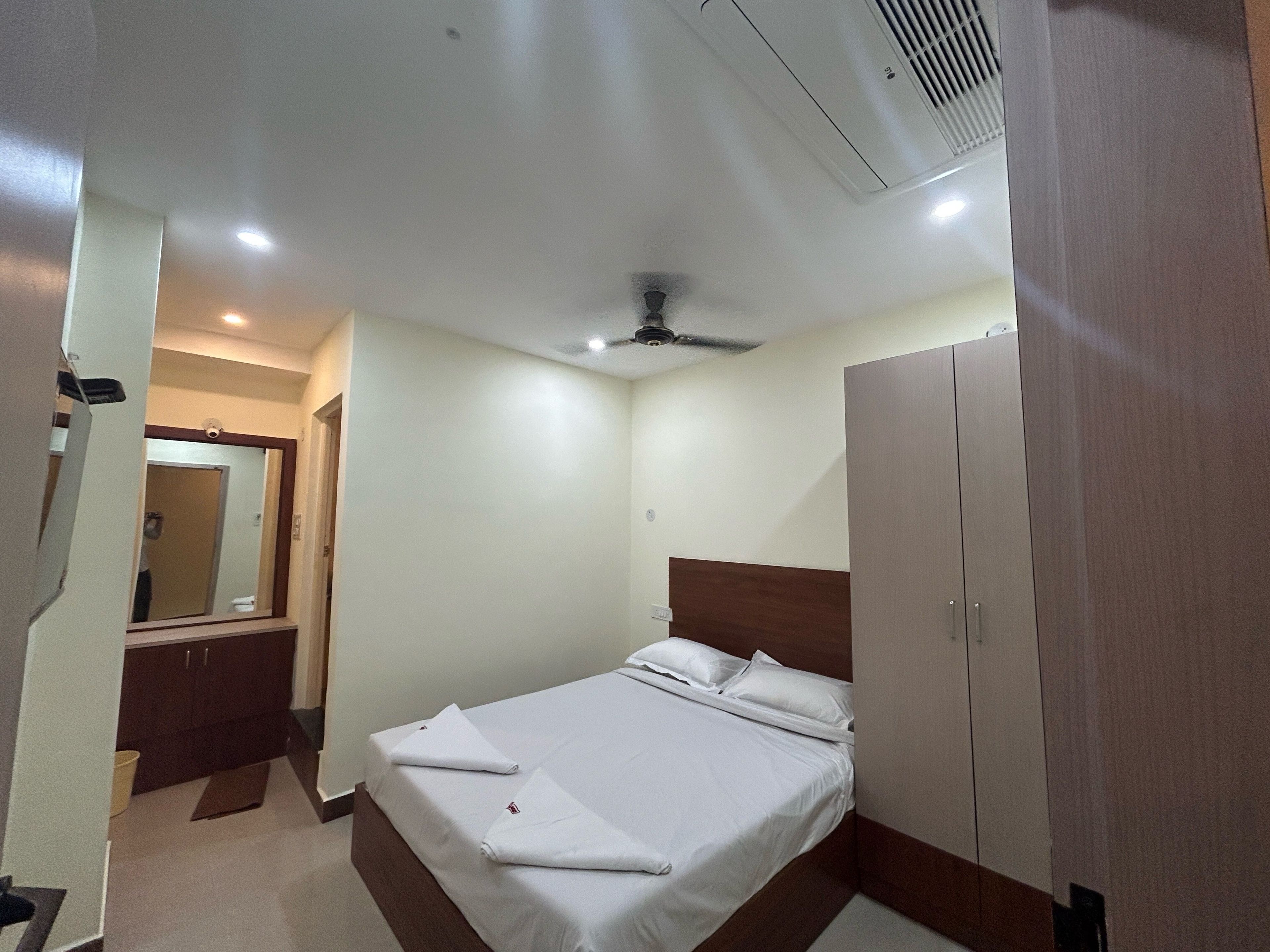A hotel room with a bed, a wardrobe, a mirror, and a ceiling fan.