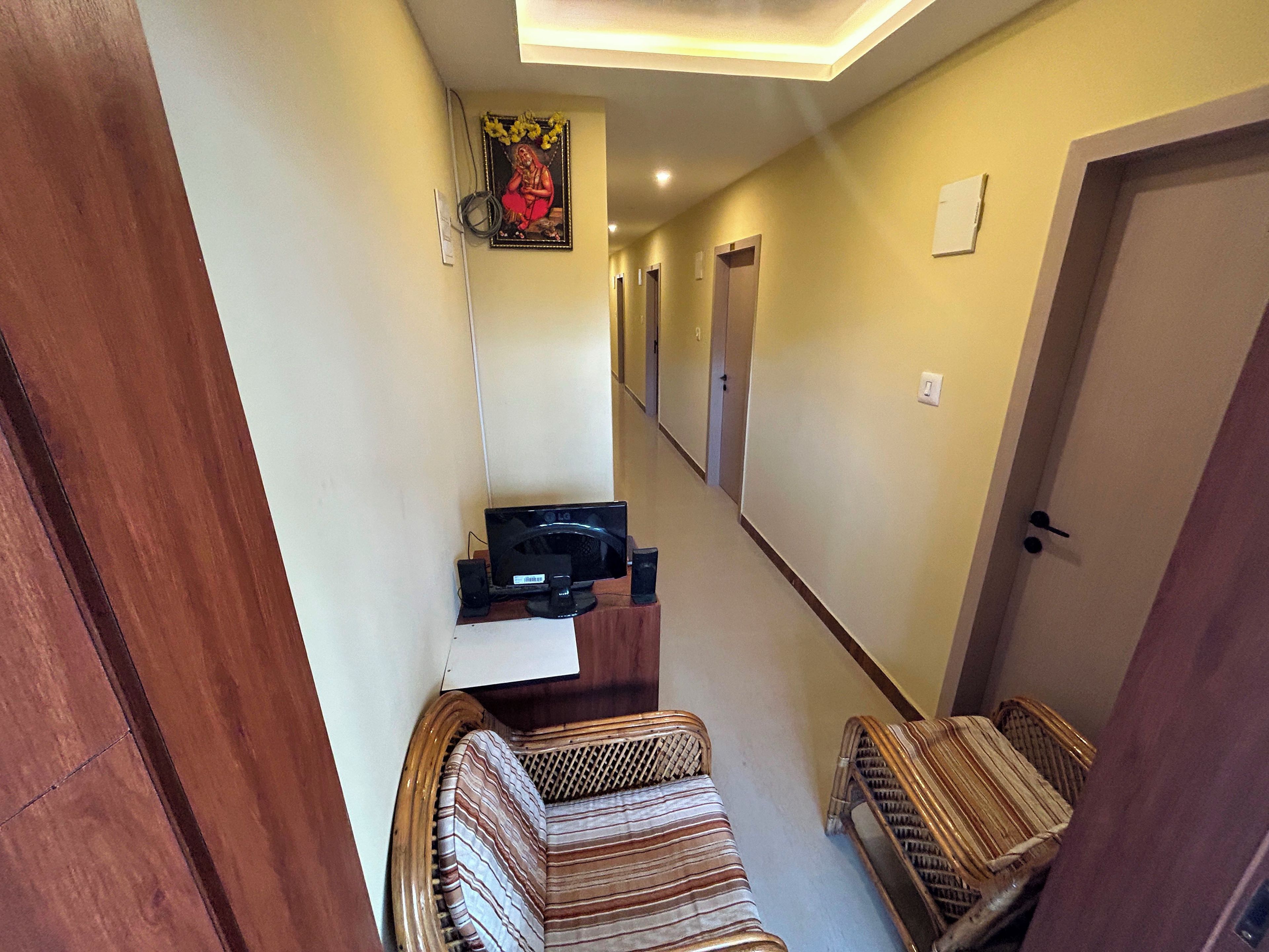A narrow hallway with a sofa and two wicker chairs, a television, and a framed picture on the wall.