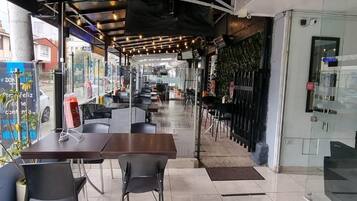 Een terras met tafels en stoelen, een glazen wand en uitzicht op de straat.