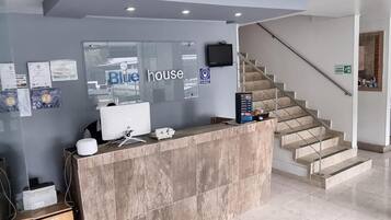 Een receptiebalie met een bord waarop 'Blue House' staat, een computer en certificaten aan de muur.