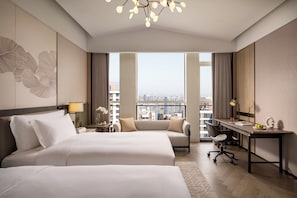 Habitación de hotel con dos camas, un escritorio, una silla y vistas a la ciudad.