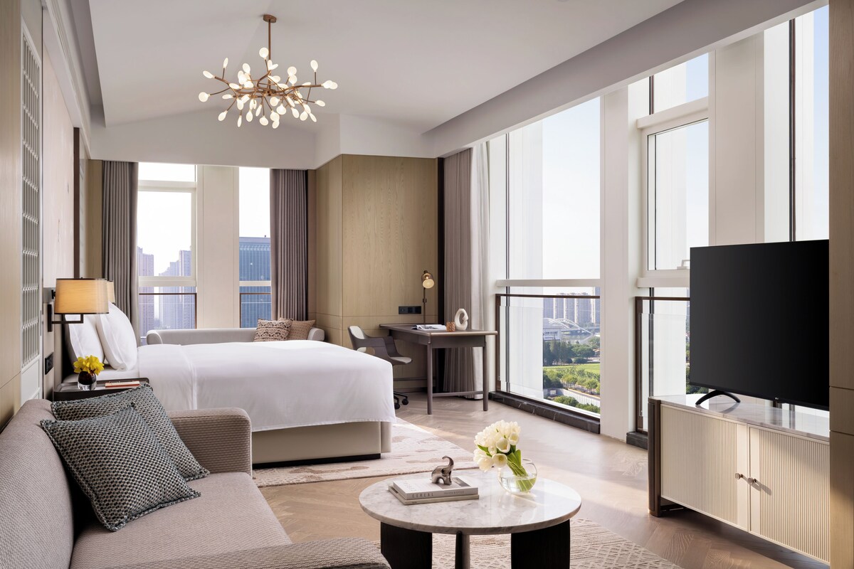 Una habitación de hotel moderna con una cama grande, un sofá, un escritorio, un televisor y vistas a la ciudad.