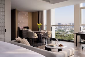 Habitación de hotel moderna con una cama grande, un área de descanso con una mesita de café, un escritorio y vistas a la ciudad.