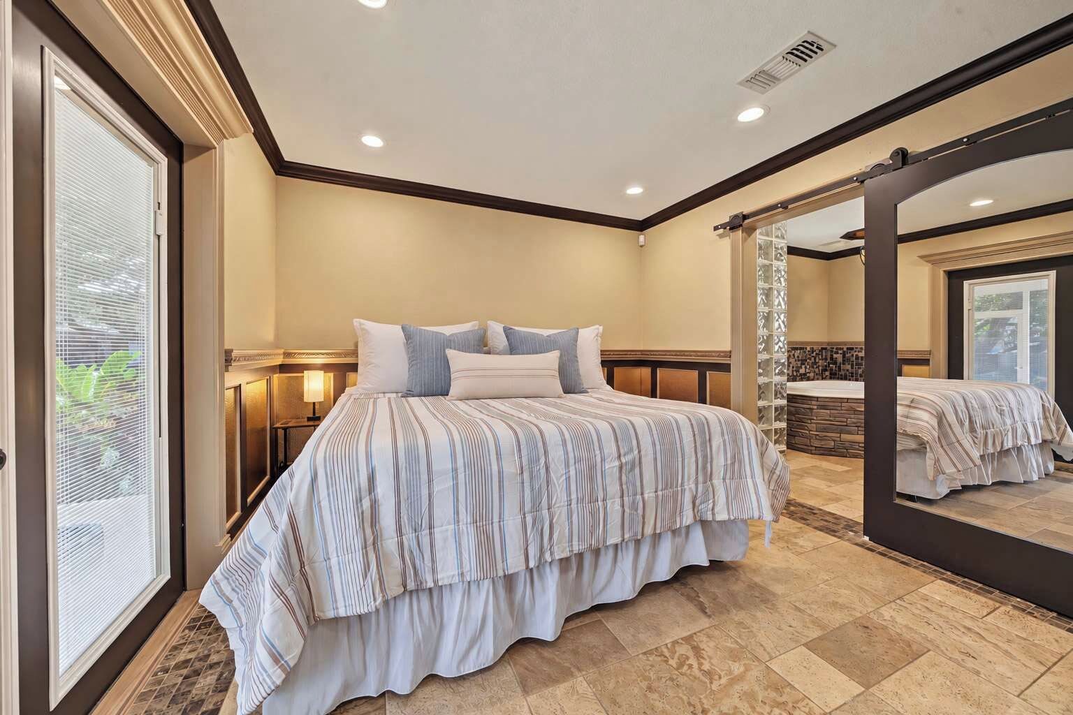 Une chambre à coucher avec un grand lit, une table de chevet, un miroir et une vue sur une salle de bain avec une baignoire.