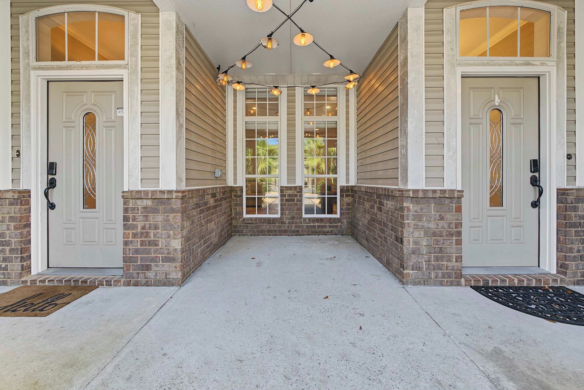 A covered porch with two doors, a brick wall, and a concrete floor.