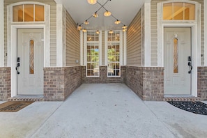 A covered porch with two doors, a brick wall, and a concrete floor. - Pelican Pointe - a 2BR part of a duplex that sleeps 6 (Pensacola)